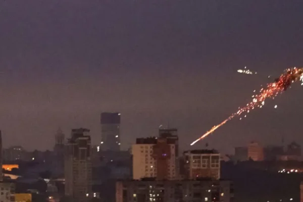 Kyiv skyline at night under Russian aerial bombardment with explosions and anti-aircraft fire, showing widespread attack.