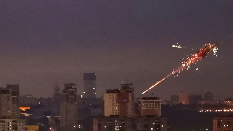 Kyiv skyline at night under Russian aerial bombardment with explosions and anti-aircraft fire, showing widespread attack.
